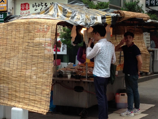 Pochangmacha (포장마차) - food cart. This particular one specialized in spicy rice cakes and fried fishcakes kabobs. Notice the happy (& friendly) customer waving as I took this photo! :D